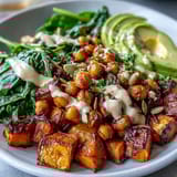 Golden roasted sweet potatoes and crispy chickpeas are served over spinach with a smoky chipotle tahini dressing on this wholesome bowl.