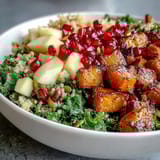 A finished Kale Harvest Grain Bowl topped with pomegranate seeds and a tangy homemade dressing, ready to serve.