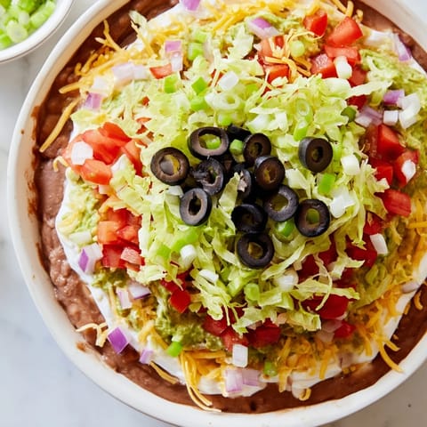 Looking at a vibrant Seven-Layer Dip, ready to be scooped up with crunchy tortilla chips for sharing.