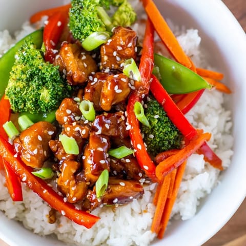 Steaming teriyaki chicken bowl piled high with tender chicken and sprinkled with sesame seeds.