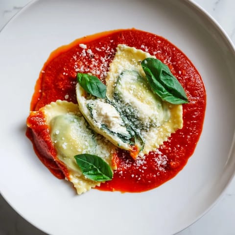 Golden, perfectly sealed ravioli filled with creamy ricotta and spinach, served on a white plate with glistening red sauce.