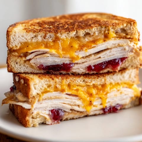 A perfectly grilled Smoked Turkey Grilled Cheese sandwich, sliced to reveal layers of juicy smoked turkey, rich cheddar, and tangy cranberry sauce on crispy bread.  