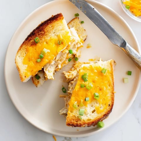 A close-up of a Buffalo Chicken Ranch Grilled Cheese, buttery bread toasted golden brown, gooey cheese stretching between two savory halves.