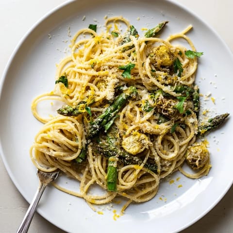 A close-up of a vibrant spring pasta dish showcasing the Roasted Garlic & Asparagus Pasta garnished with fresh parsley and lemon zest.  
