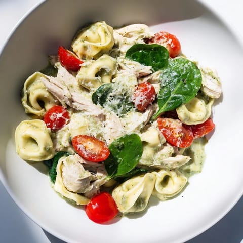 Creamy Pesto Tortellini Skillet with tender pasta, shredded chicken, and wilted spinach in a bubbling green sauce.