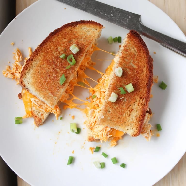 Sliced Buffalo Chicken Ranch Grilled Cheese sandwich served with fresh celery sticks, highlighting the spicy buffalo chicken and creamy ranch filling.