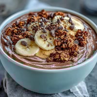 Two bowls of Chunky Monkey Smoothie Bowls show thick chocolatey smoothie topped with banana slices, granola, cacao nibs, and hemp seeds for a healthy breakfast.