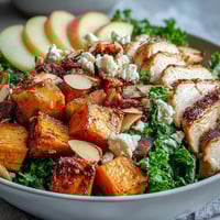 Golden roasted chicken and caramelized sweet potatoes top a bed of massaged kale in this Fall Sweet Potato Harvest Bowl, garnished with crisp apple slices and crumbled goat cheese.  